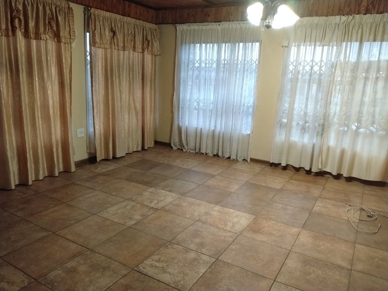 An empty living room featuring ceramic floor tiles, wooden ceiling trim, and large windows fitted with security gates.