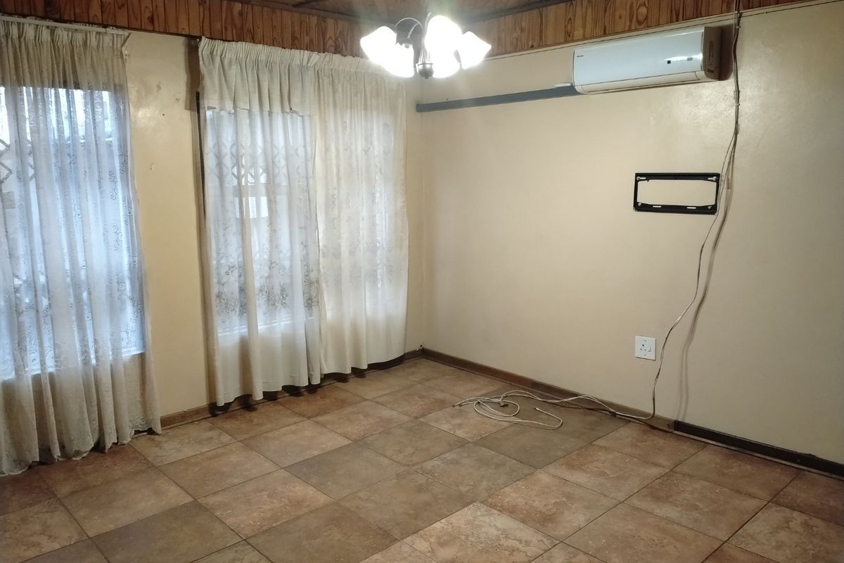 An empty living room featuring tiled flooring, wooden ceiling paneling, and a wall-mounted air conditioning unit.