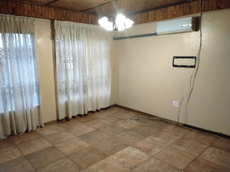An empty living room featuring tiled flooring, wooden ceiling paneling, and a wall-mounted air conditioning unit.
