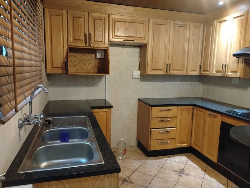 A functional kitchen featuring oak cabinetry, granite countertops, a double bowl sink, and built-in oven with extractor fan, finished with tiled flooring.