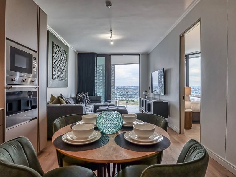 Modern open-plan living and dining area featuring integrated kitchen appliances, laminate flooring, and seamless access to a private balcony with scenic views.