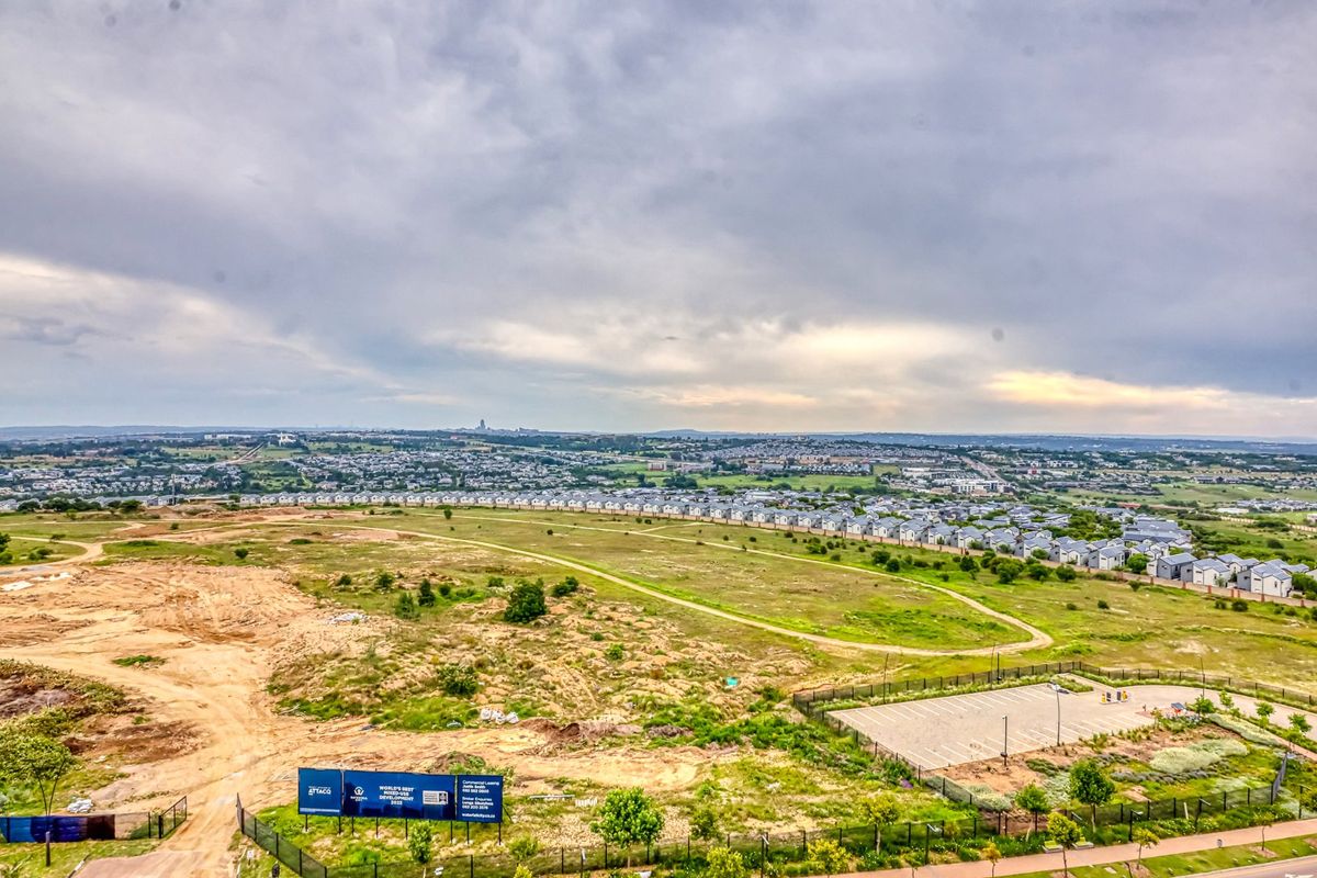 An elevated aerial view of the surrounding estate, featuring open land, residential housing clusters, and a paved parking area.