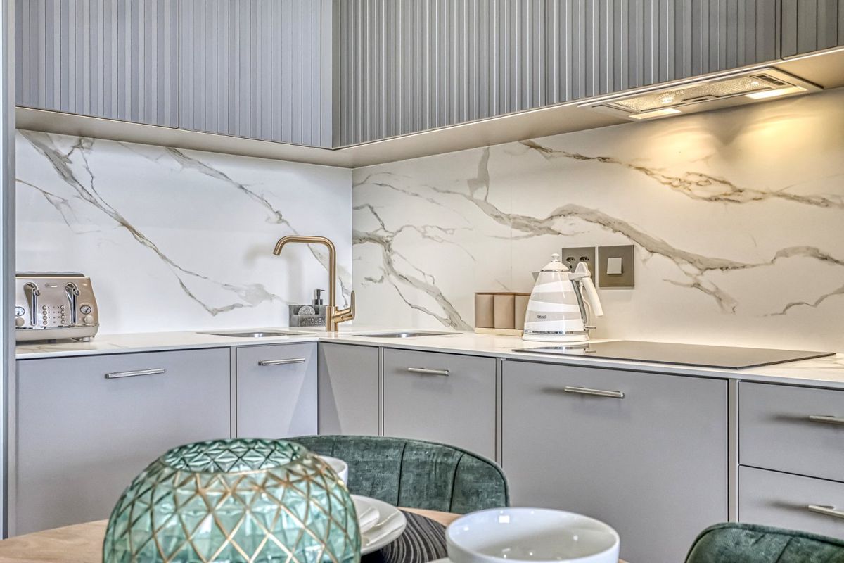 Modern kitchen featuring fluted grey cabinetry, marble-look splashback, brass faucet, and integrated hob with sleek under-cabinet lighting.
