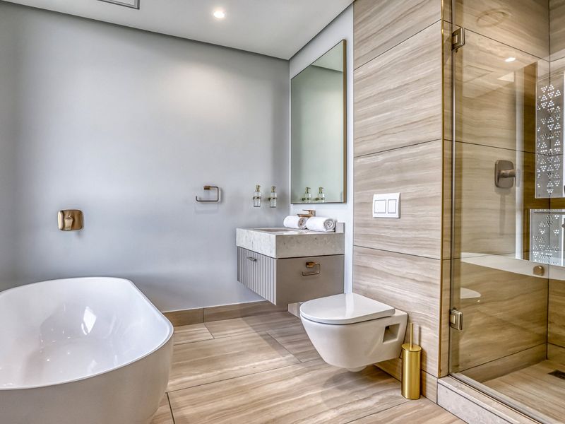 Modern bathroom featuring a sleek freestanding bathtub, wall-hung toilet, floating vanity with stone countertop, and a spacious glass-enclosed shower with contemporary finishes.