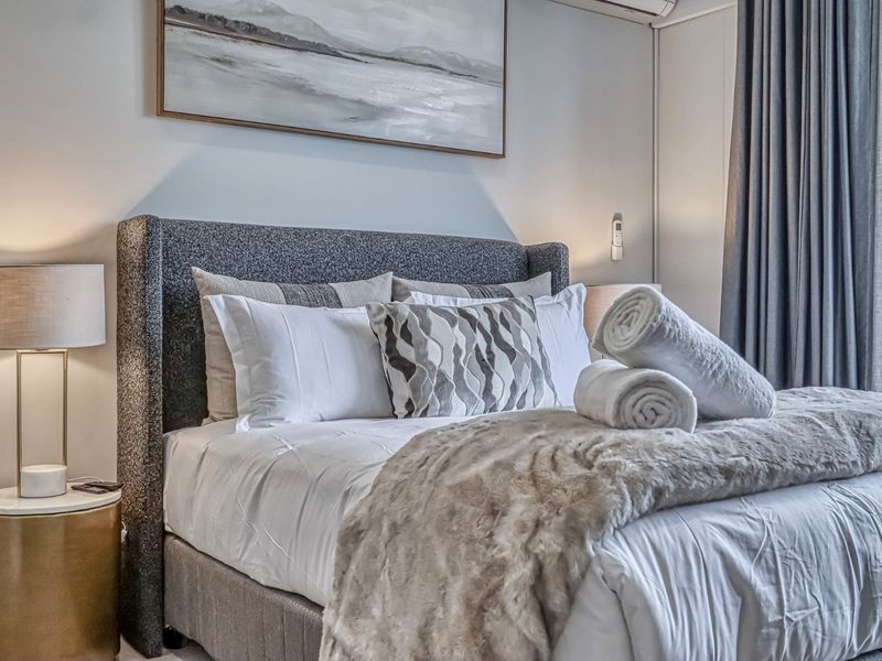 A well-appointed bedroom featuring neutral tones, modern wall-mounted air conditioning, and floor-to-ceiling curtains, creating a comfortable and inviting living space.