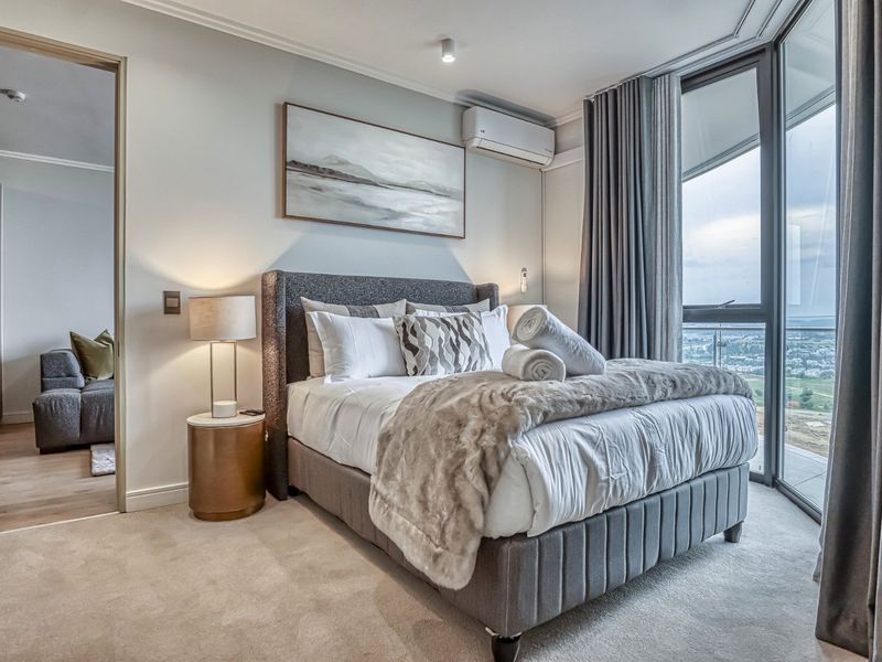 Modern bedroom featuring plush carpeting, split-system air conditioning, and floor-to-ceiling windows with expansive views and access to a private balcony.