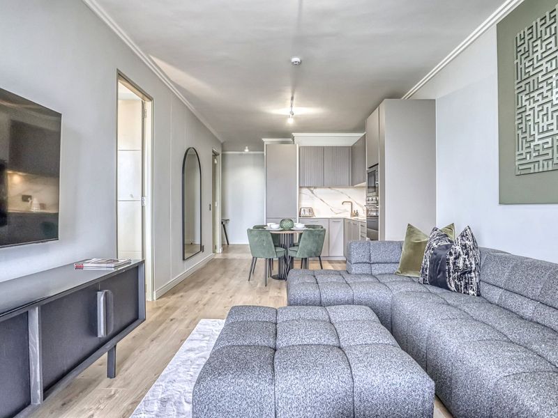 Modern open-plan living area featuring a sleek kitchen with integrated appliances, light wood-look flooring, and neutral finishes throughout.