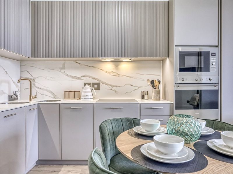 Modern open-plan kitchen featuring sleek grey cabinetry, marble-look splashback, integrated appliances, and high-end brass fixtures, seamlessly flowing into the dining area.