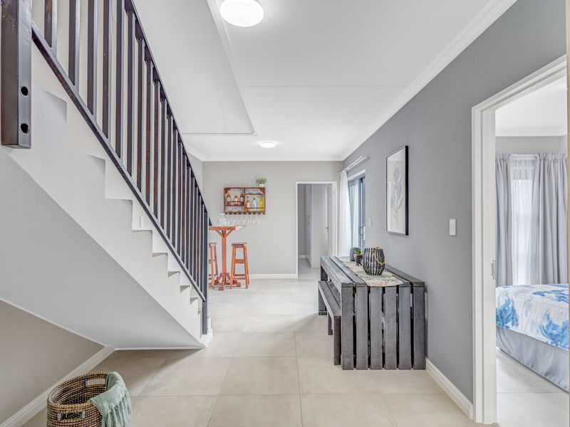 A bright and spacious hallway featuring neutral tiled flooring, a modern staircase with dark railings, and clean grey wall finishes.
