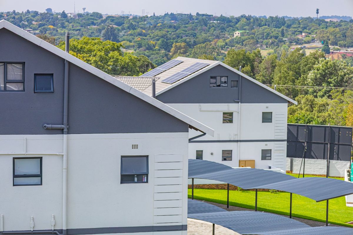 Exterior view of townhouse complex featuring modern grey and white facades, solar panels, and covered carport parking areas.