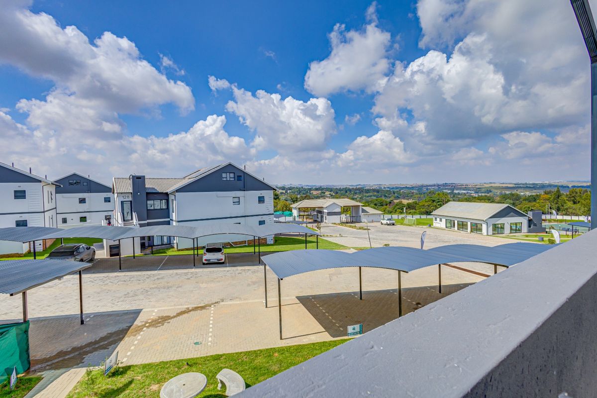 An elevated view of the townhouse complex featuring paved parking areas, covered carports, and well-maintained communal grounds under a clear sky.