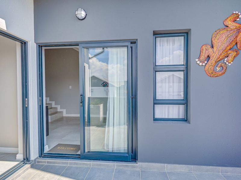A clean, modern patio area featuring tiled flooring, a sliding glass door entrance, and an exterior wall light.