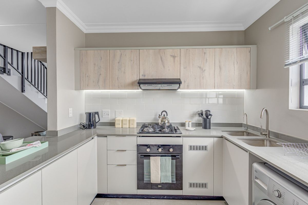 Modern kitchen featuring light wood-tone upper cabinets, white lower cabinetry, stone countertops, gas hob, built-in oven, and a subway tile backsplash.