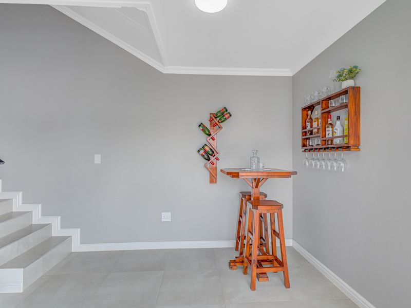 A neat bar area featuring tiled flooring and a staircase, finished with clean grey walls and decorative cornice detailing.