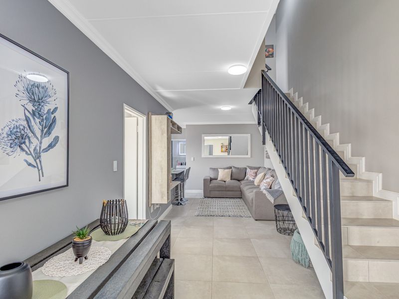 Open-plan living area featuring a modern staircase with metal balustrade, neutral tiled flooring, and recessed ceiling lighting in a well-maintained townhouse interior.
