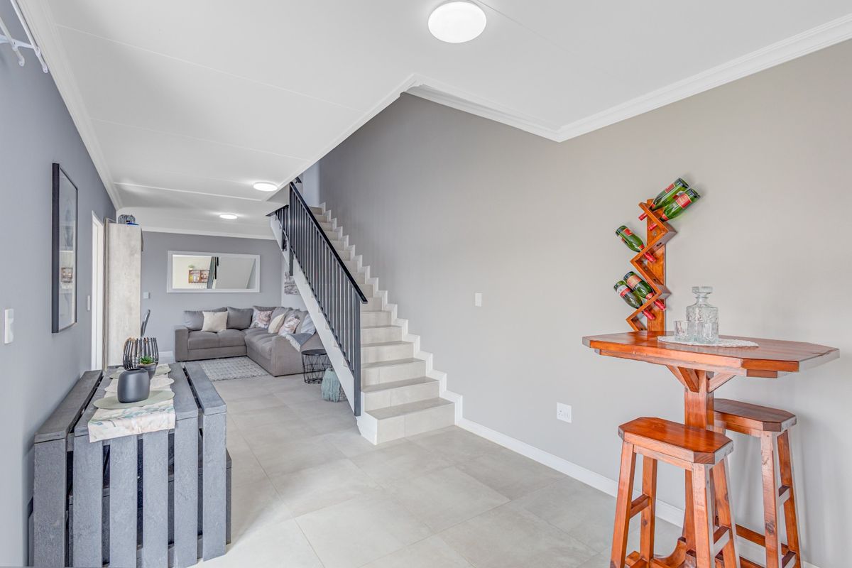 Open-plan living area featuring tiled flooring, a central staircase with a modern balustrade, and neutral wall finishes with recessed lighting.