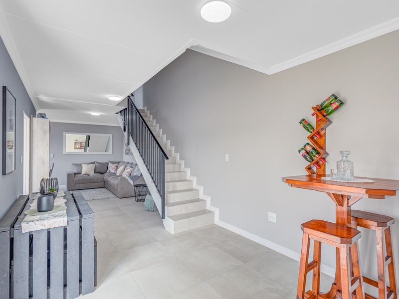 Open-plan living area featuring tiled flooring, a central staircase with a modern balustrade, and neutral wall finishes with recessed lighting.
