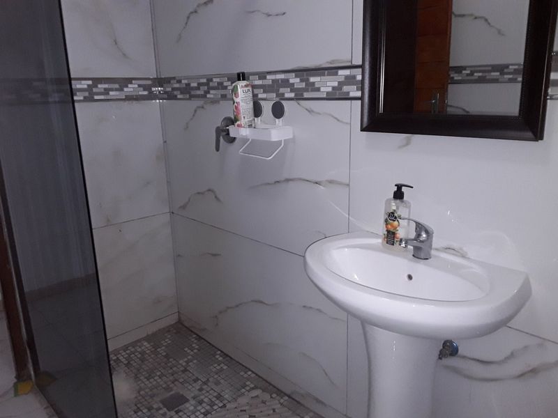 A modern bathroom featuring marble-look wall tiles, a pedestal basin with a mixer tap, and a glass-enclosed shower area with mosaic floor tiling.
