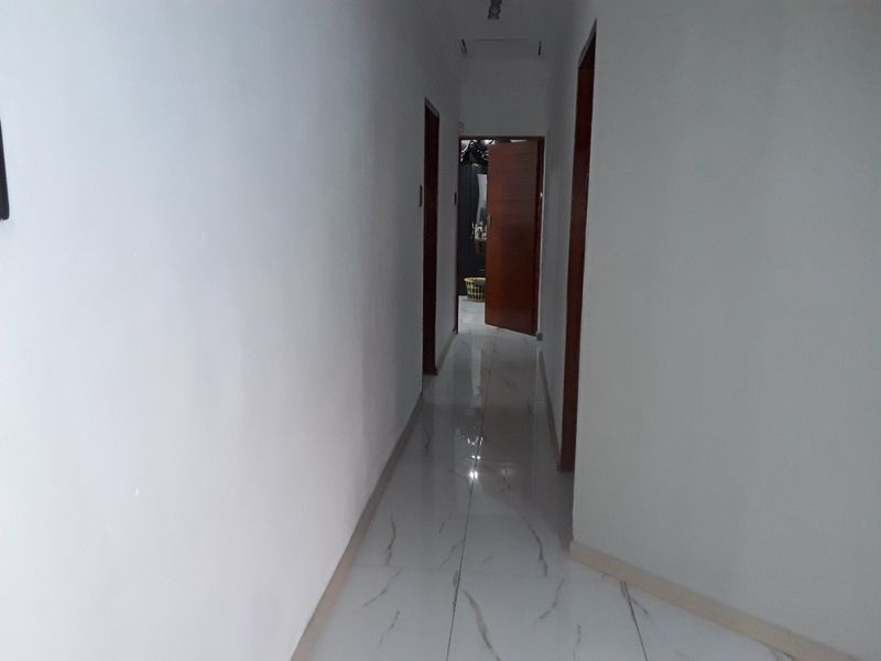 A simple, clean hallway featuring white walls and light-colored tiled flooring with dark veining, connecting multiple rooms within the home.