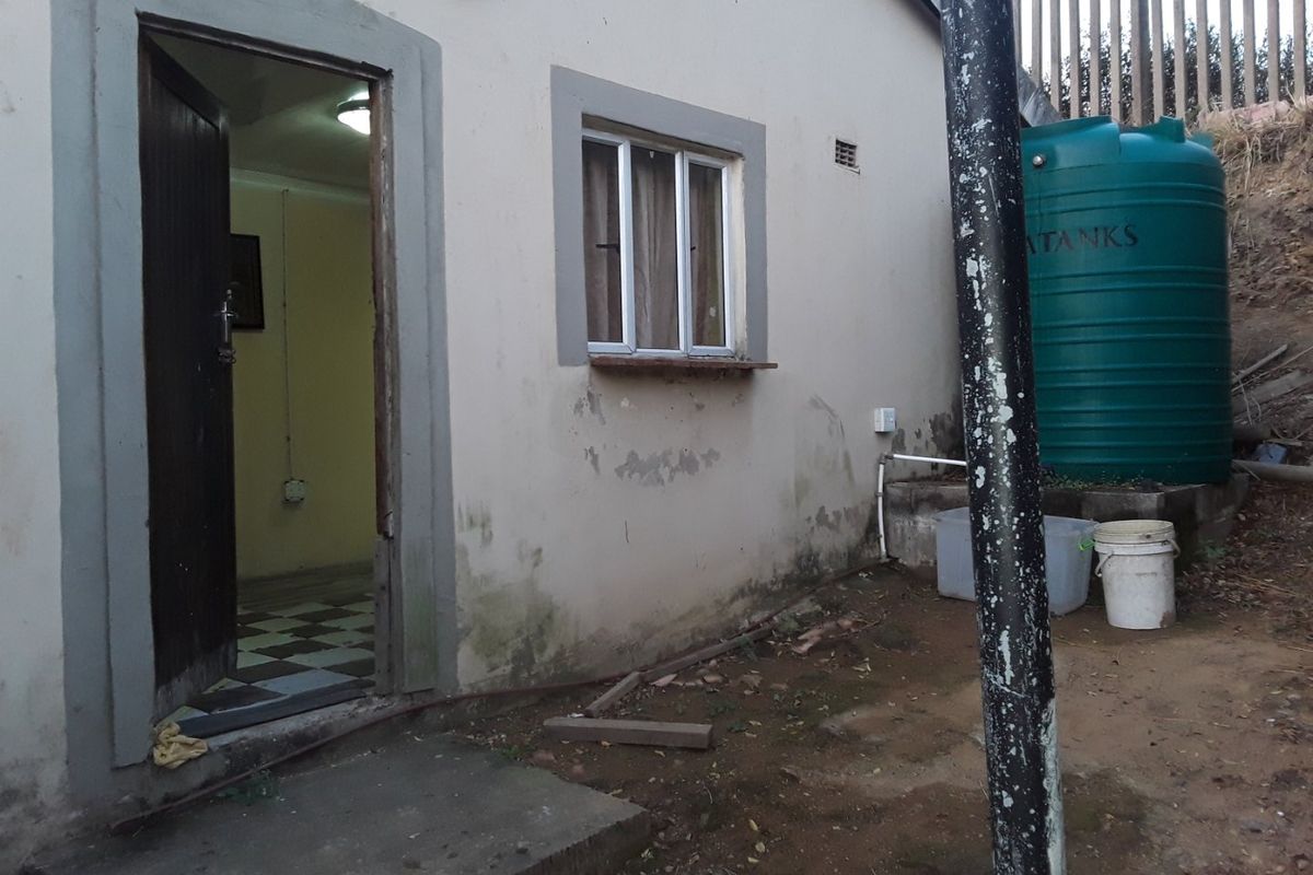 Rear exterior view of the property showing a water storage tank, concrete step, and visible wear to the exterior wall finish.