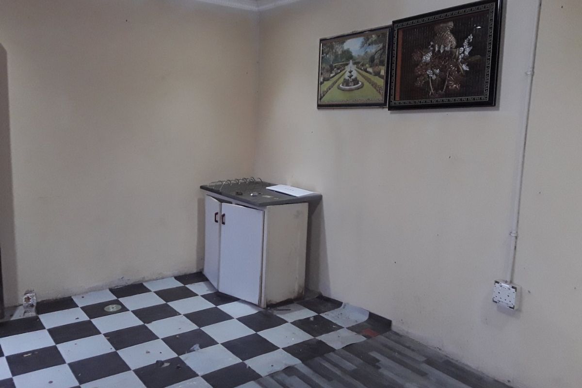 A small, dated kitchen area featuring mismatched flooring, basic built-in cabinetry, and a single countertop unit, requiring significant renovation and cosmetic updates.