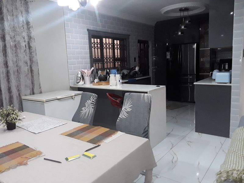 Modern open-plan kitchen and dining area featuring glossy cabinetry, subway tile backsplash, and polished porcelain floor tiles with integrated breakfast bar.
