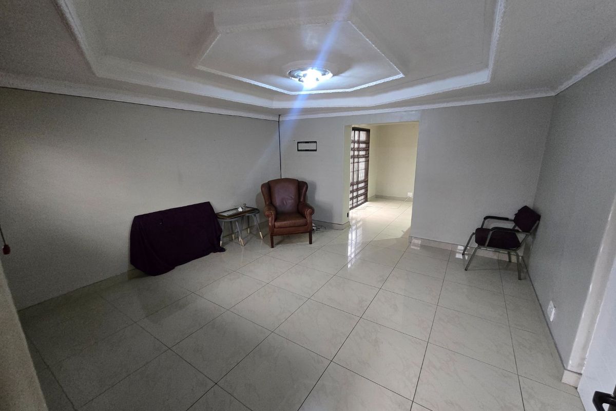 A spacious living area featuring large format floor tiles and a decorative recessed tray ceiling, leading through to a secure entrance area.