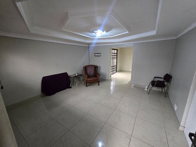 A spacious living area featuring large format floor tiles and a decorative recessed tray ceiling, leading through to a secure entrance area.