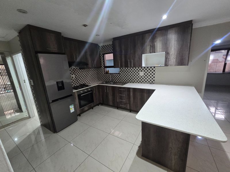 Modern kitchen featuring dark wood cabinetry, white stone countertops, a gas hob, built-in oven, and tiled flooring in an open-plan layout.