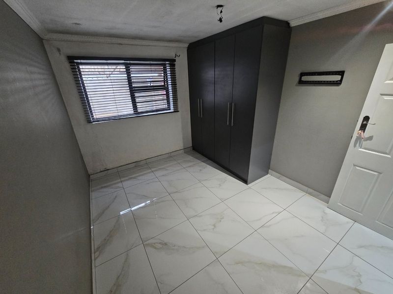 An empty bedroom featuring modern white marble-look floor tiles, a dark built-in wardrobe, and venetian blinds.