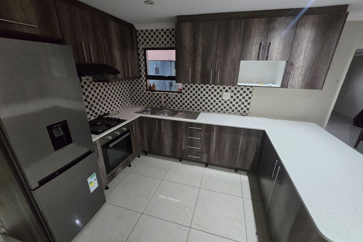 Modern kitchen featuring dark wood-grain cabinetry, white quartz countertops, a mosaic tile backsplash, and integrated stainless steel appliances.
