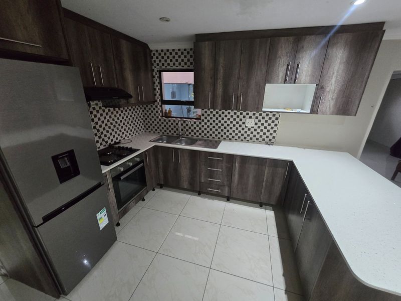 Modern kitchen featuring dark wood-grain cabinetry, white quartz countertops, a mosaic tile backsplash, and integrated stainless steel appliances.
