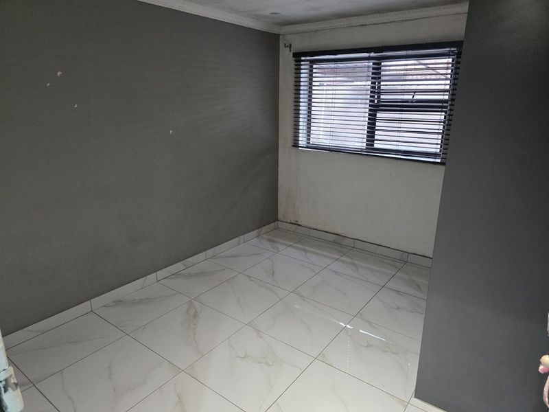 An empty bedroom featuring modern marble-look floor tiles, neutral grey and white walls, and fitted venetian blinds.