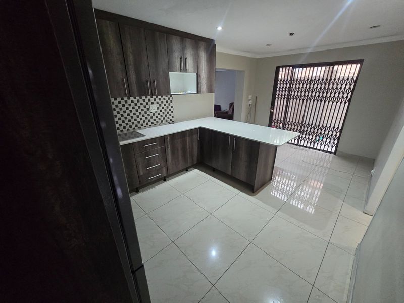 Modern kitchen featuring dark wood-finish cabinetry, white countertops, tiled backsplash, and ceramic flooring, leading to an outdoor area secured by a metal gate.