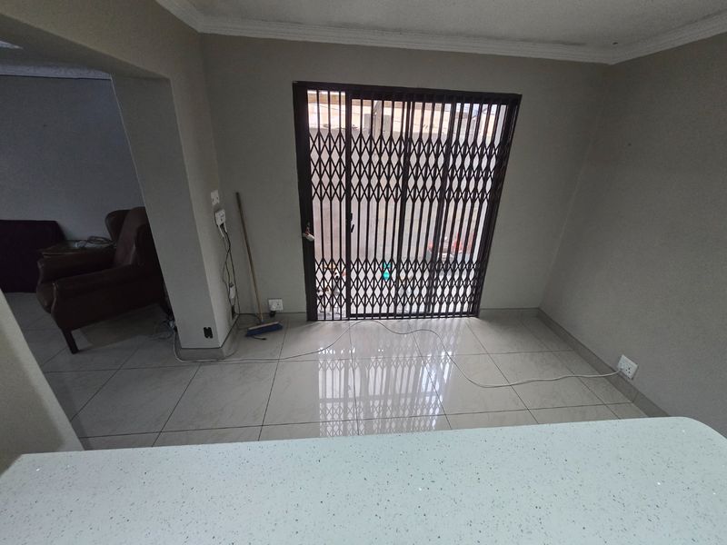 An open-plan living area featuring tiled flooring, a sliding glass door with a security gate, and neutral wall finishes.
