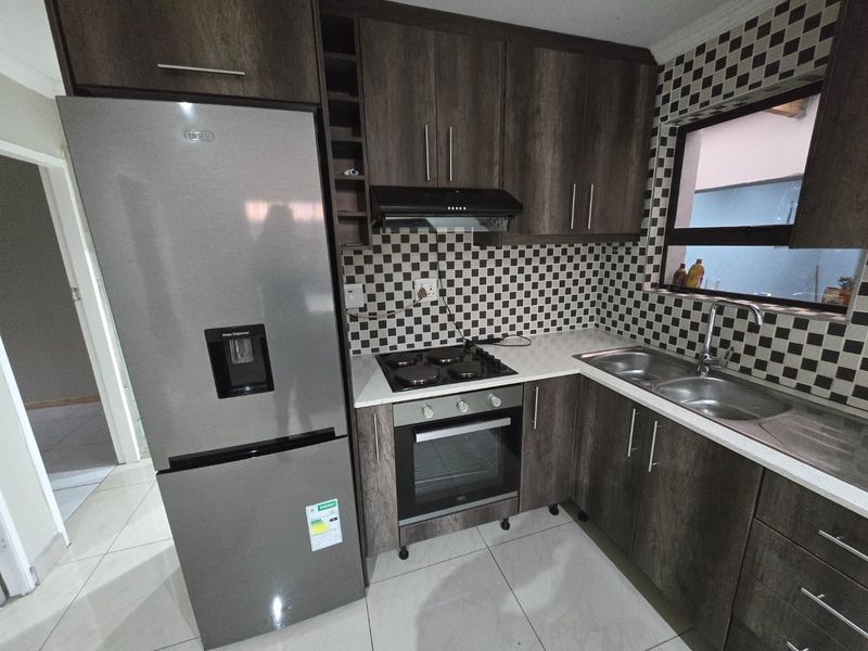 A functional kitchen featuring dark wood-look cabinetry, a built-in oven and hob, extractor fan, double sink, and a distinctive checkered tile backsplash.