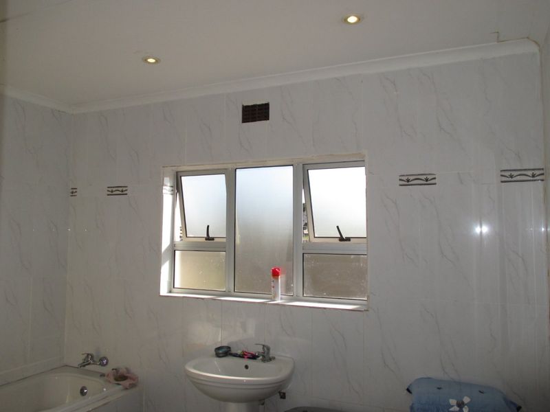 A functional bathroom featuring tiled walls, a pedestal washbasin, and a built-in bathtub with chrome fixtures.