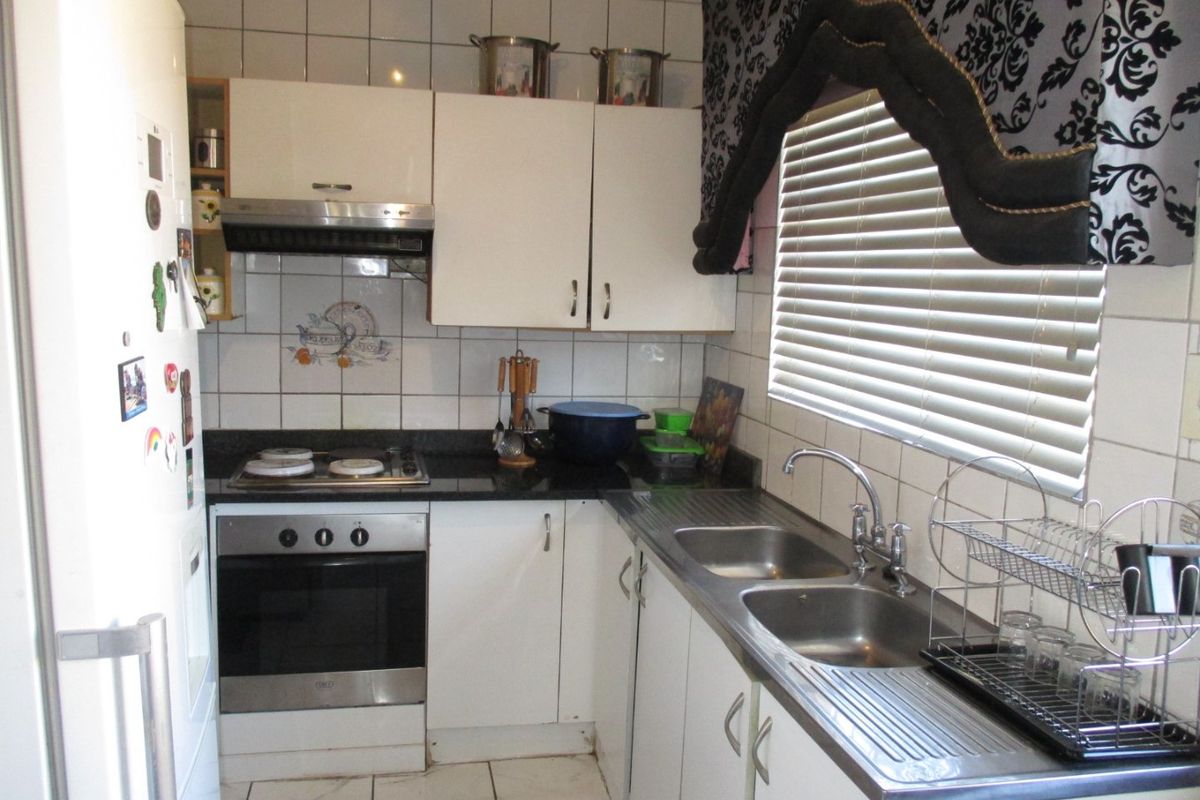 A functional kitchen featuring white cabinetry, a built-in oven with hob, extractor fan, and a double stainless steel sink with tiled backsplash.