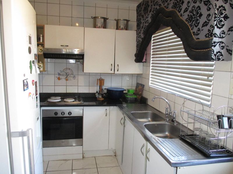 A functional kitchen featuring white cabinetry, a built-in oven with hob, extractor fan, and a double stainless steel sink with tiled backsplash.