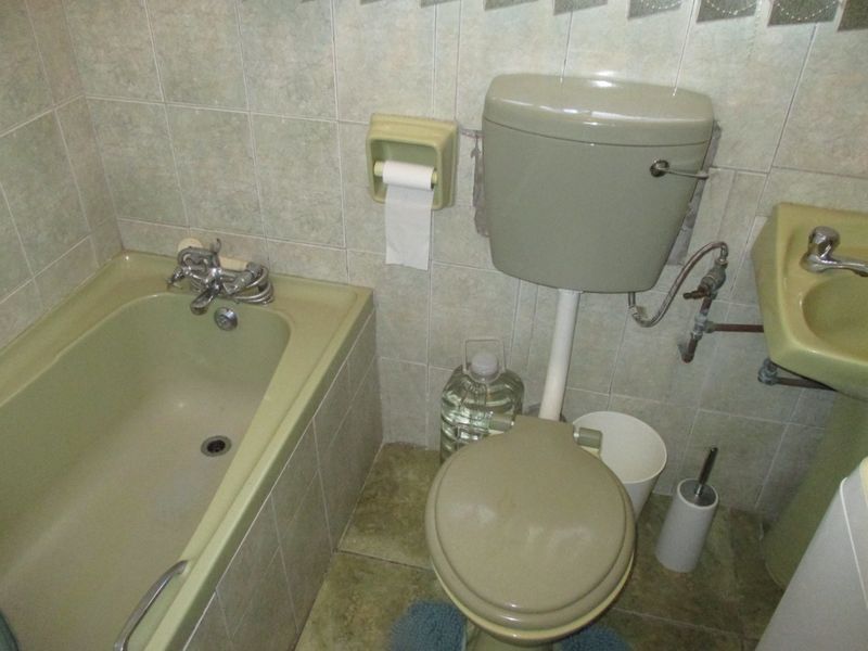 A dated bathroom featuring a vintage green suite, including a bathtub, toilet, and washbasin with tiled walls and flooring.