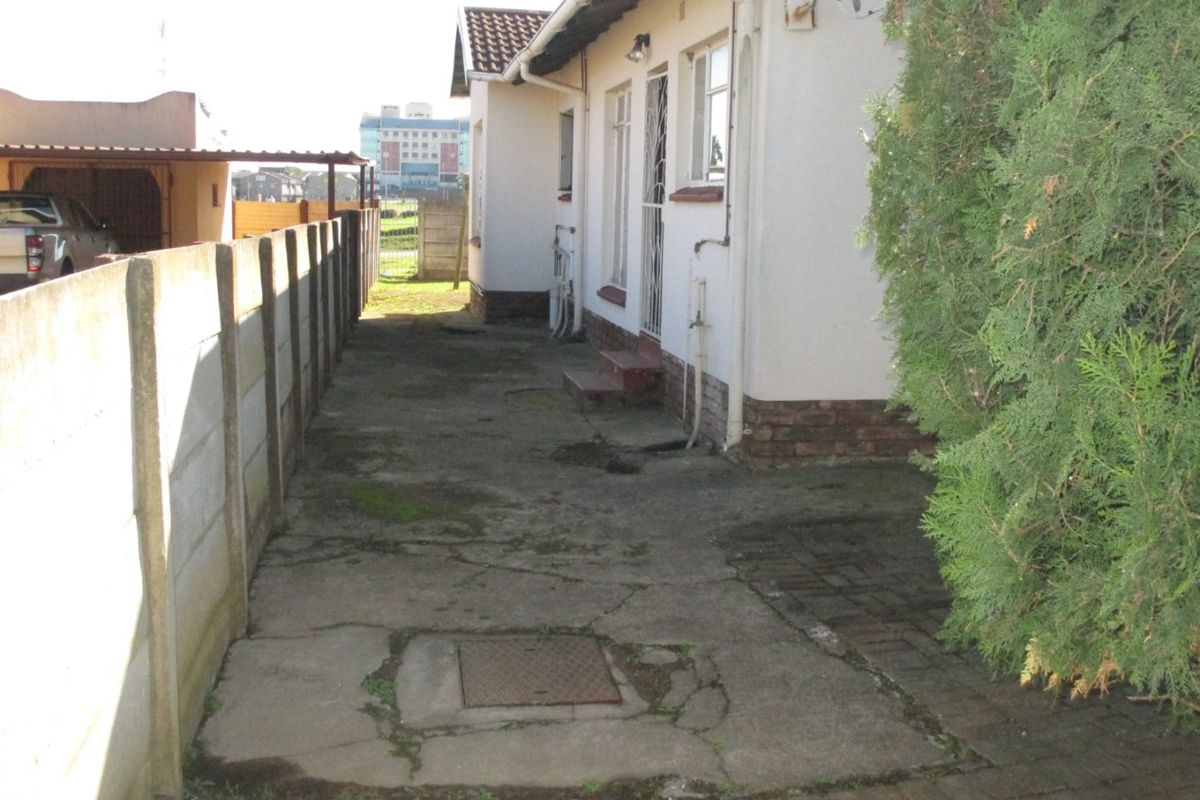 Rear exterior view of the property featuring a concrete paved walkway, boundary wall, and access to the side of the house.