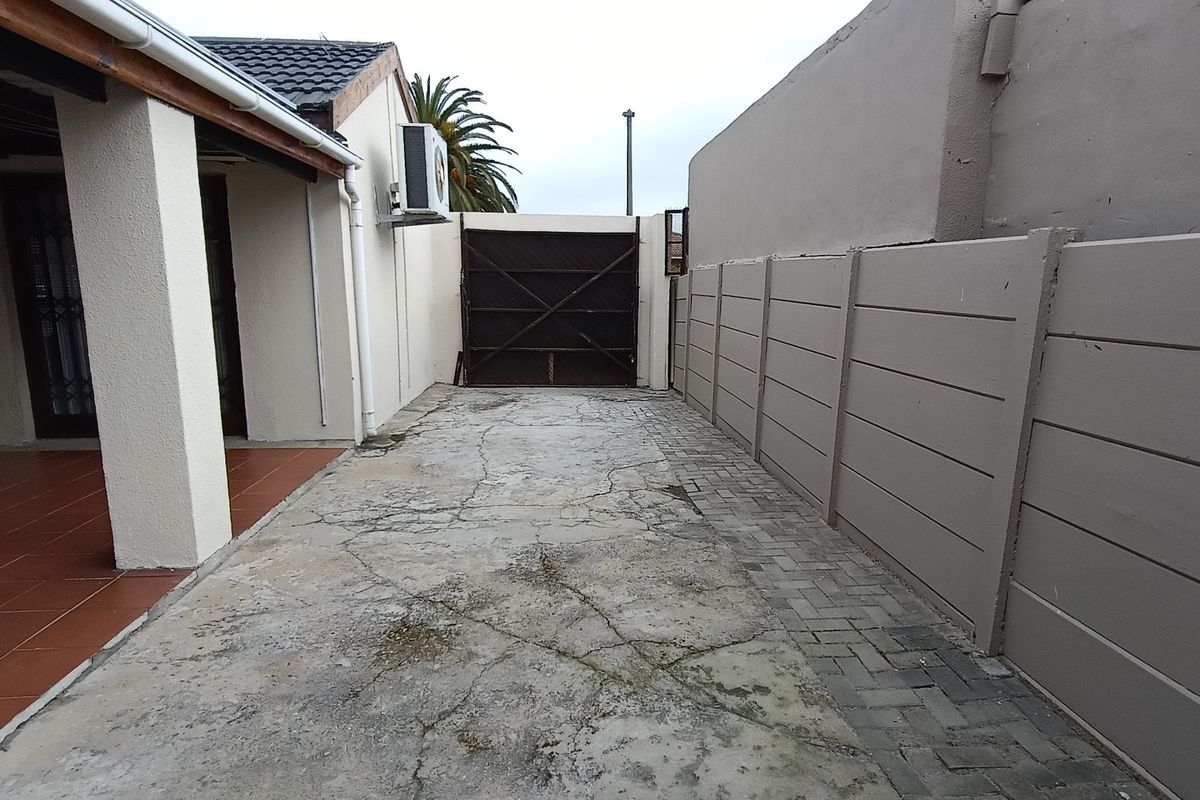 Rear exterior area featuring a tiled patio, concrete driveway with visible cracking, and a precast concrete boundary wall.