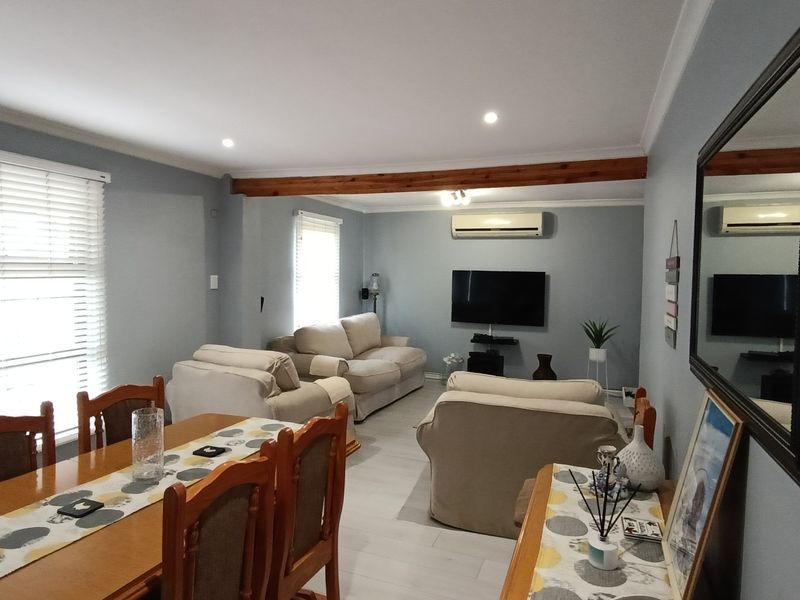 Spacious open-plan living and dining area featuring neutral tones, recessed lighting, an exposed timber beam, and a wall-mounted air conditioning unit.
