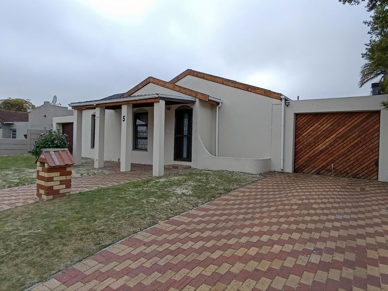 Front elevation of a single-story house featuring a paved driveway, covered entrance porch, and a wooden garage door, set within a fenced property.