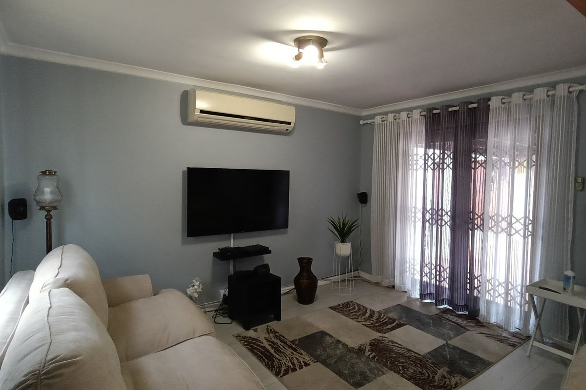 A comfortable living room featuring a wall-mounted air conditioning unit, neutral wall tones, and a sliding glass door with security gate access to the exterior.