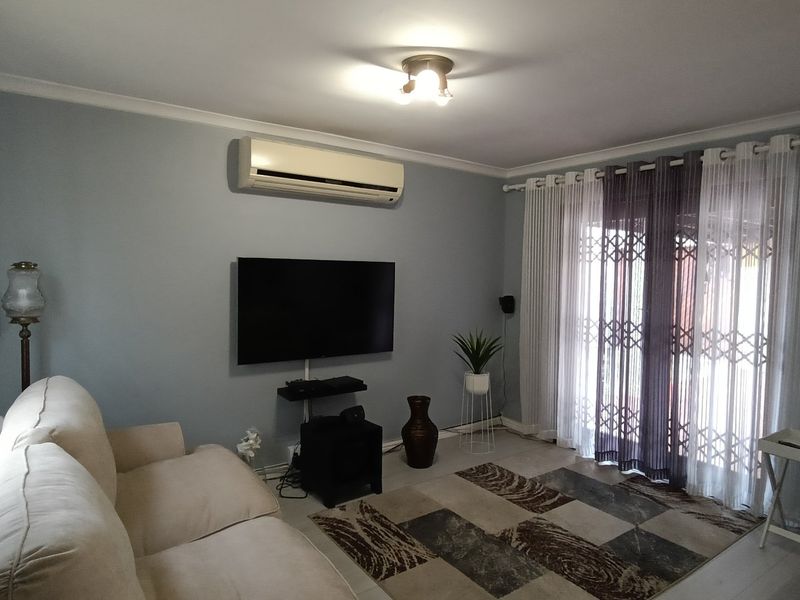A comfortable living room featuring a wall-mounted air conditioning unit, neutral wall tones, and a sliding glass door with security gate access to the exterior.