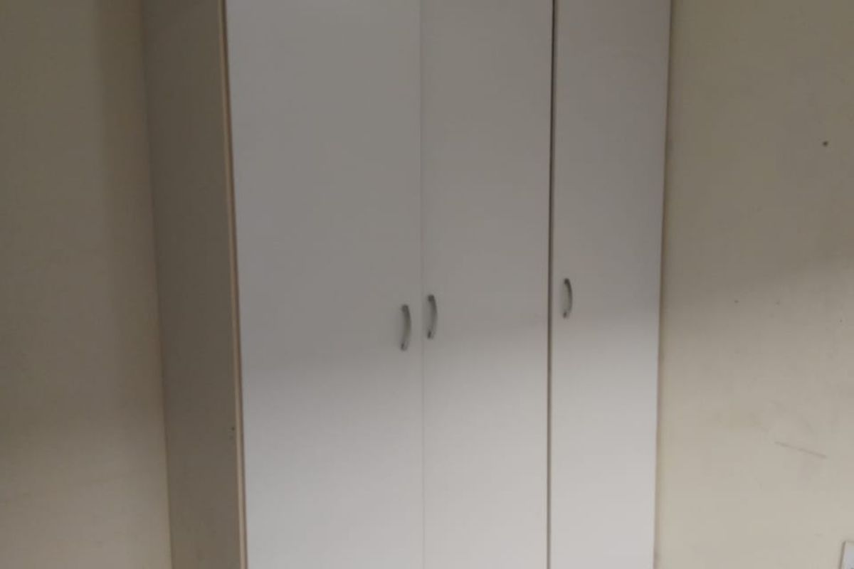 A bedroom featuring a white built-in wardrobe and neutral tiled flooring, offering a clean and functional storage solution.
