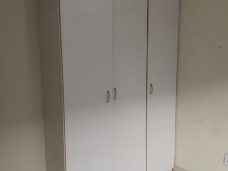 A bedroom featuring a white built-in wardrobe and neutral tiled flooring, offering a clean and functional storage solution.