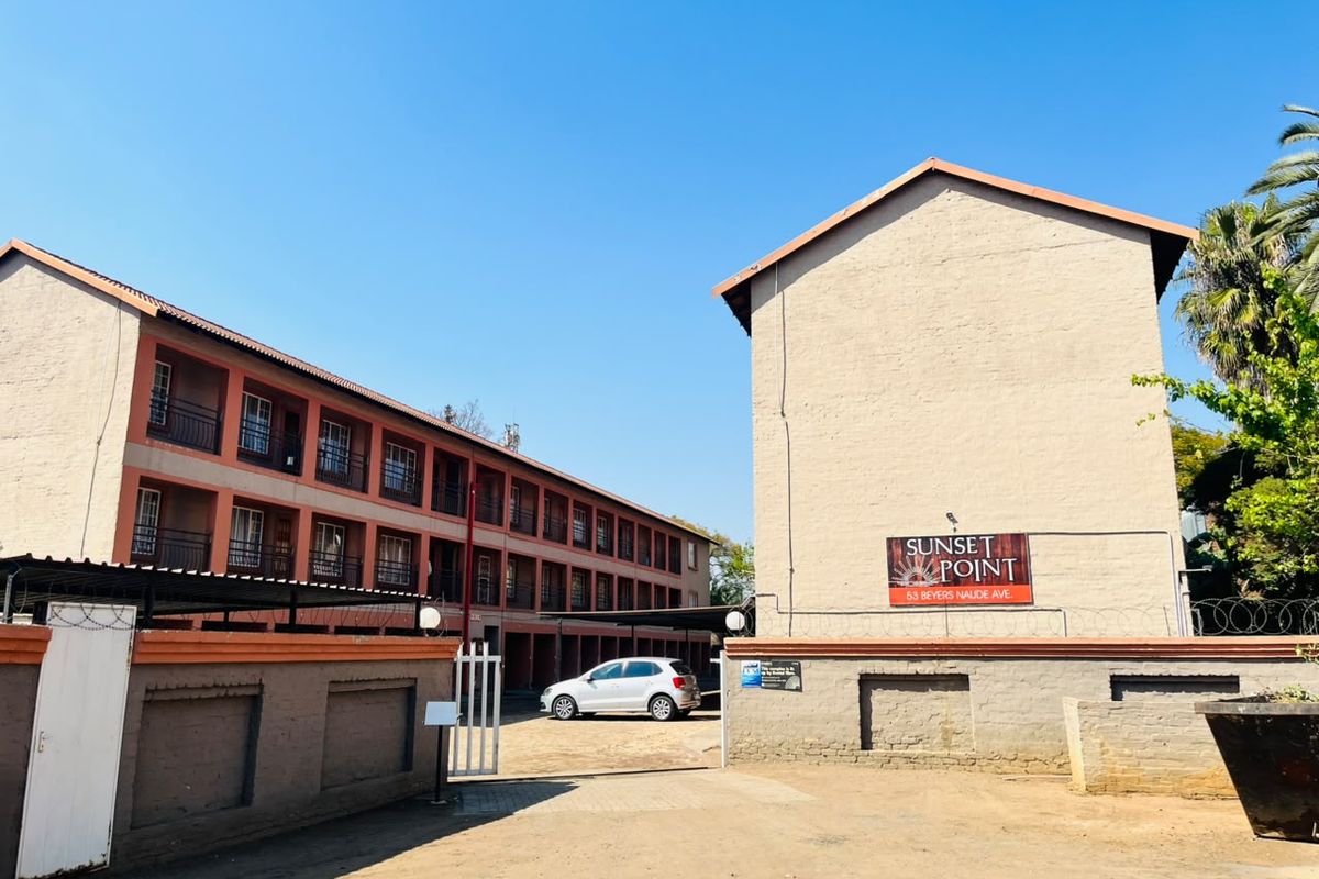 Front exterior view of the Sunset Point apartment complex, featuring multi-story residential blocks with balconies, secure perimeter walling, and gated driveway access.