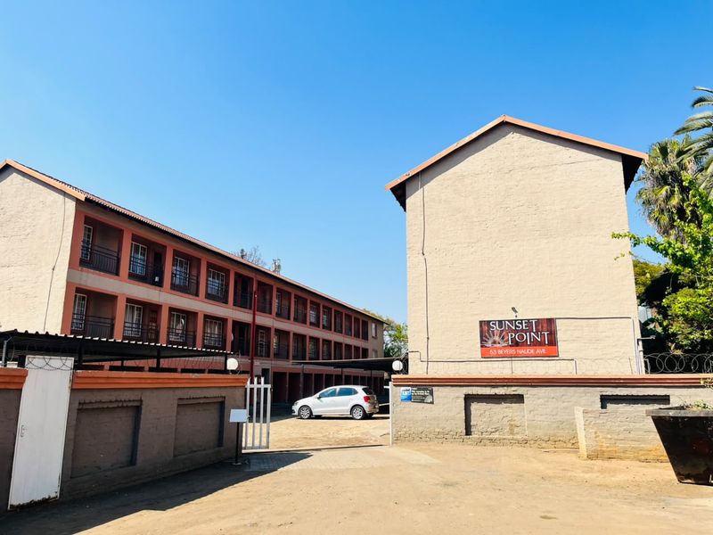 Front exterior view of the Sunset Point apartment complex, featuring multi-story residential blocks with balconies, secure perimeter walling, and gated driveway access.